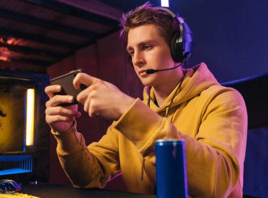 Young pro gamer playing in online mobile video games in neon coloured room