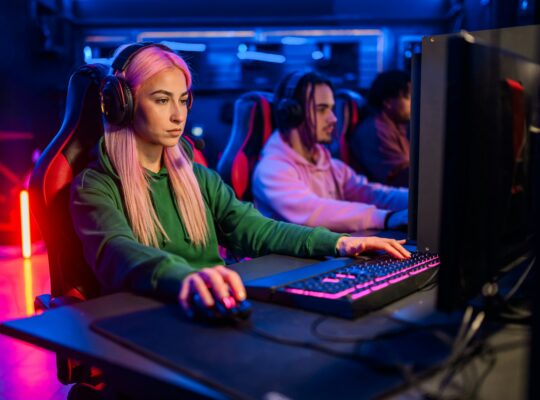 Young woman with pink hair gamer playing PC video game in a gameroom